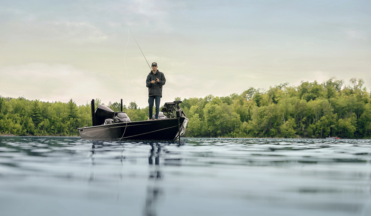 A man standing on the end of his boat with his rod in the water.