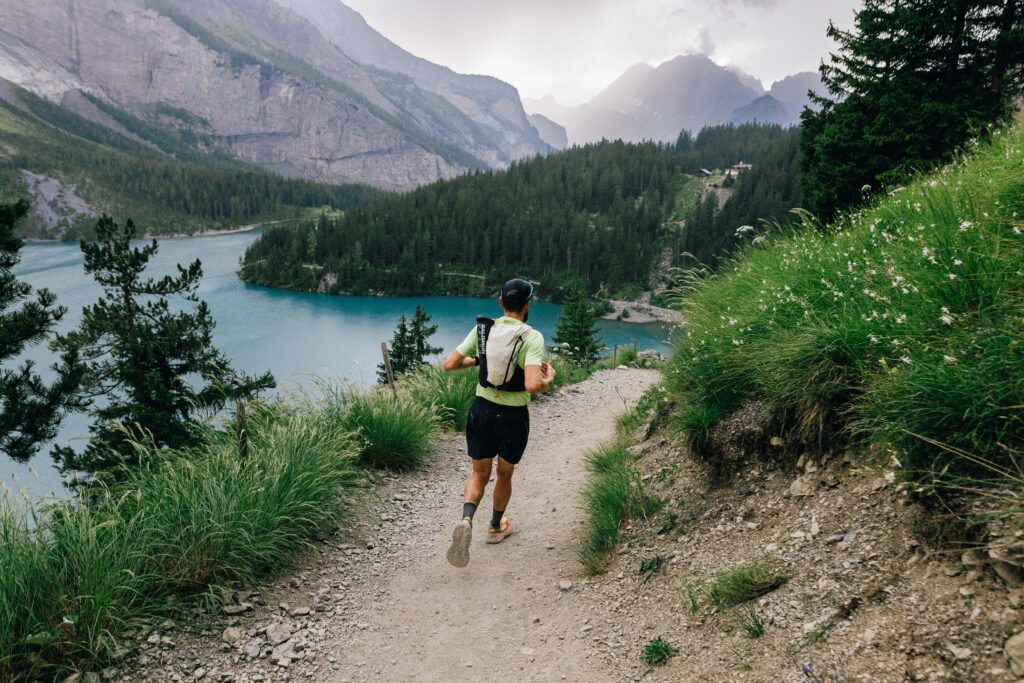 Jake Catterall runs the Via Alpina trail alongside a blue lake, with mountains in the background.