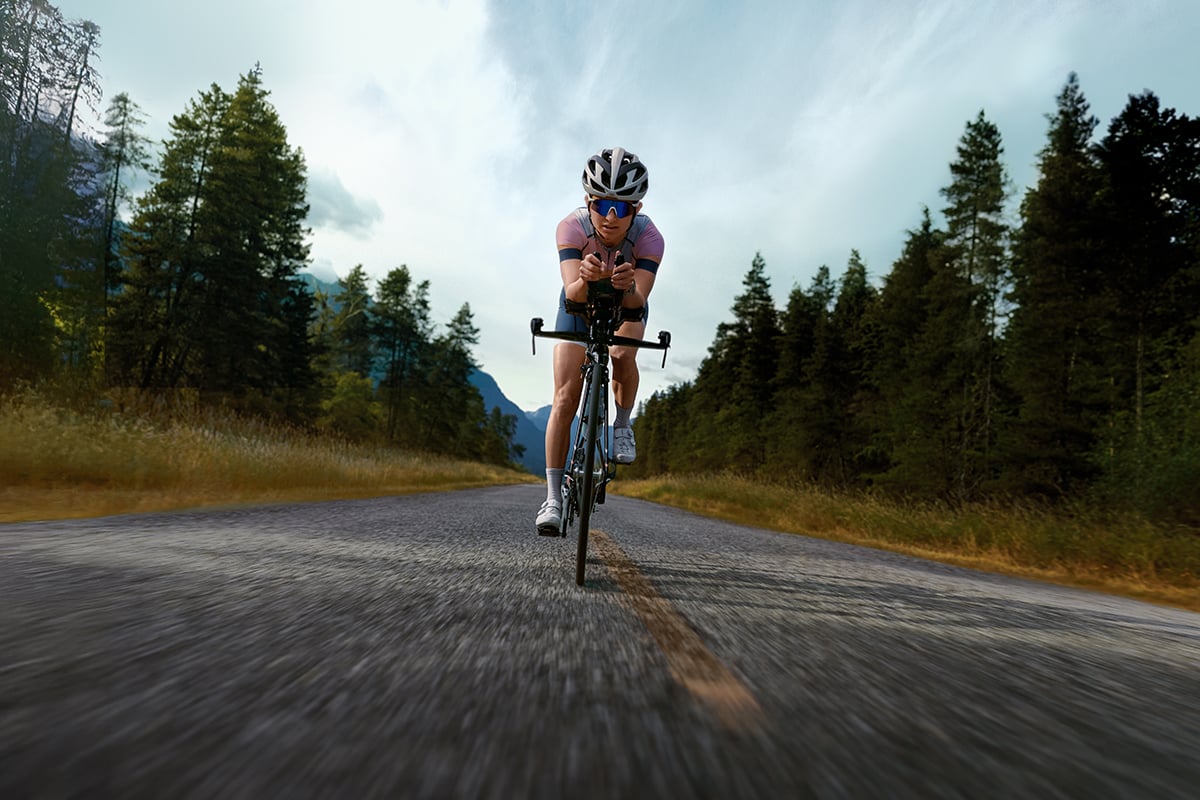 A triathlete cycles down a road lined by trees.
