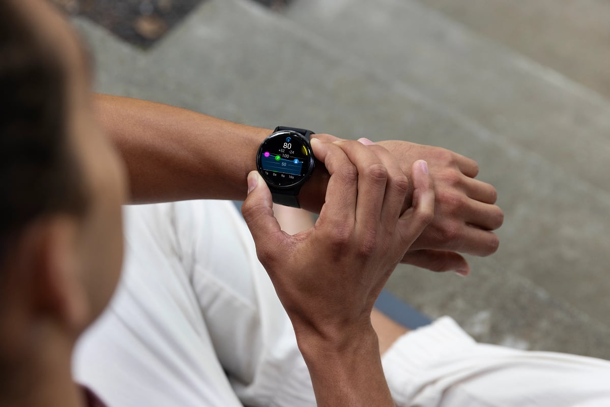A man in white pants on a gray floor checks the Body Battery feature on his Garmin Venu 3.