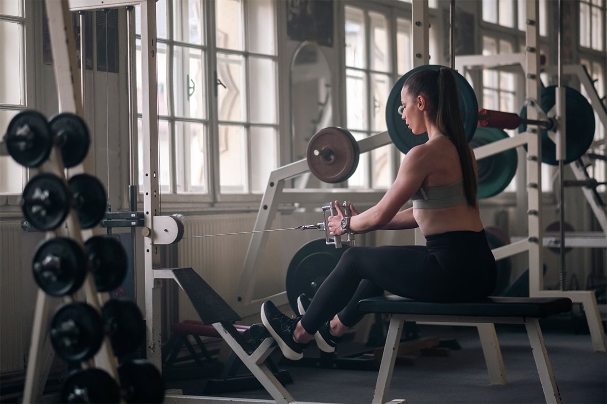 A woman wearing a Garmin fēnix 8 smartwatch works out in a gym environment.