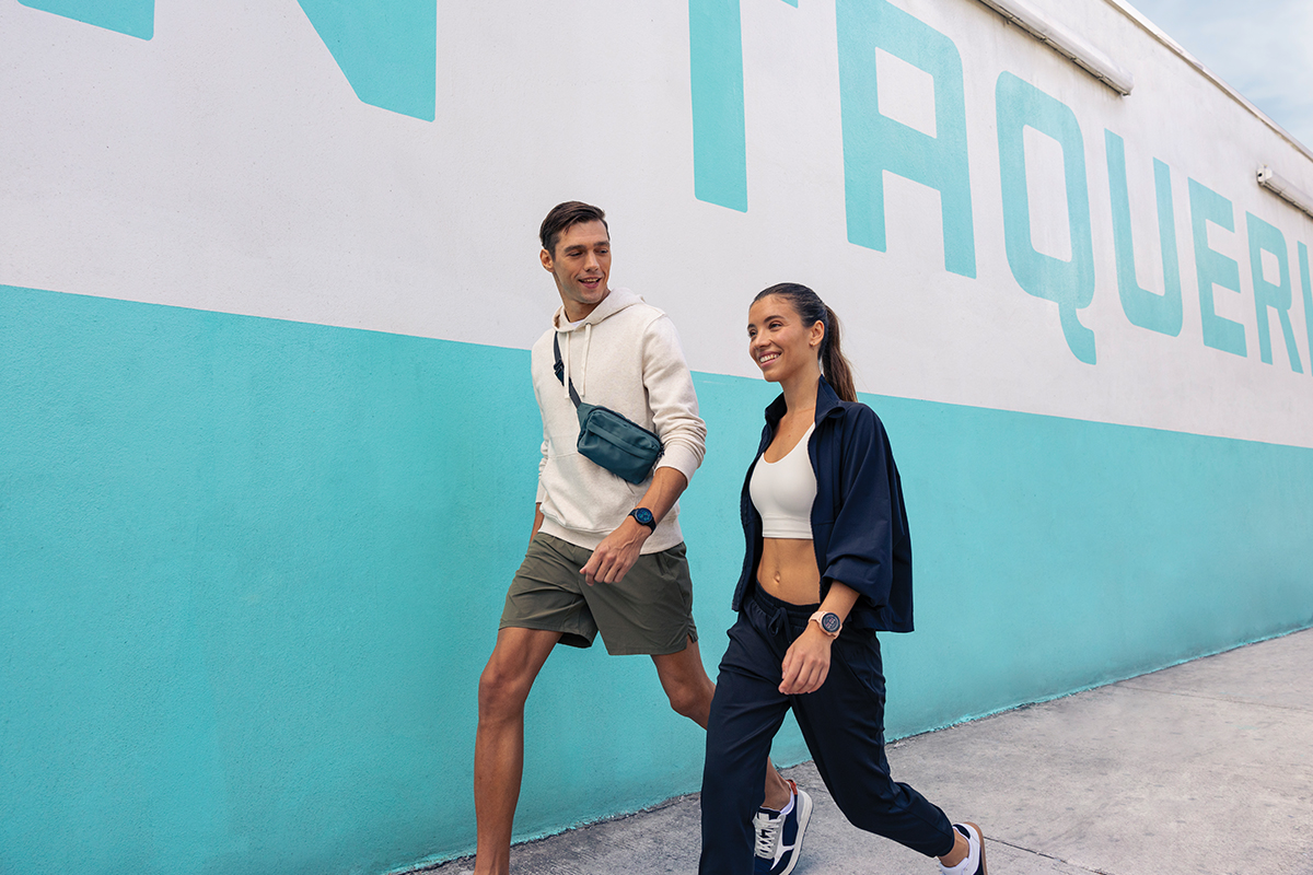 A man in a cream sweatshirt and green shorts walks next to a smiling woman wearing a navy jacket and pants.