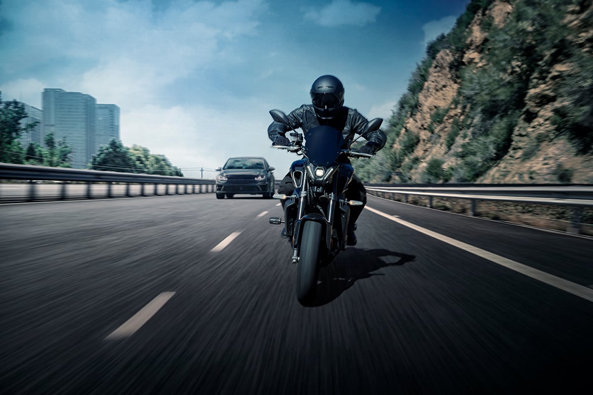 A motorcyclist using the zūmo R1 Radar rides on a road with a car in the background.