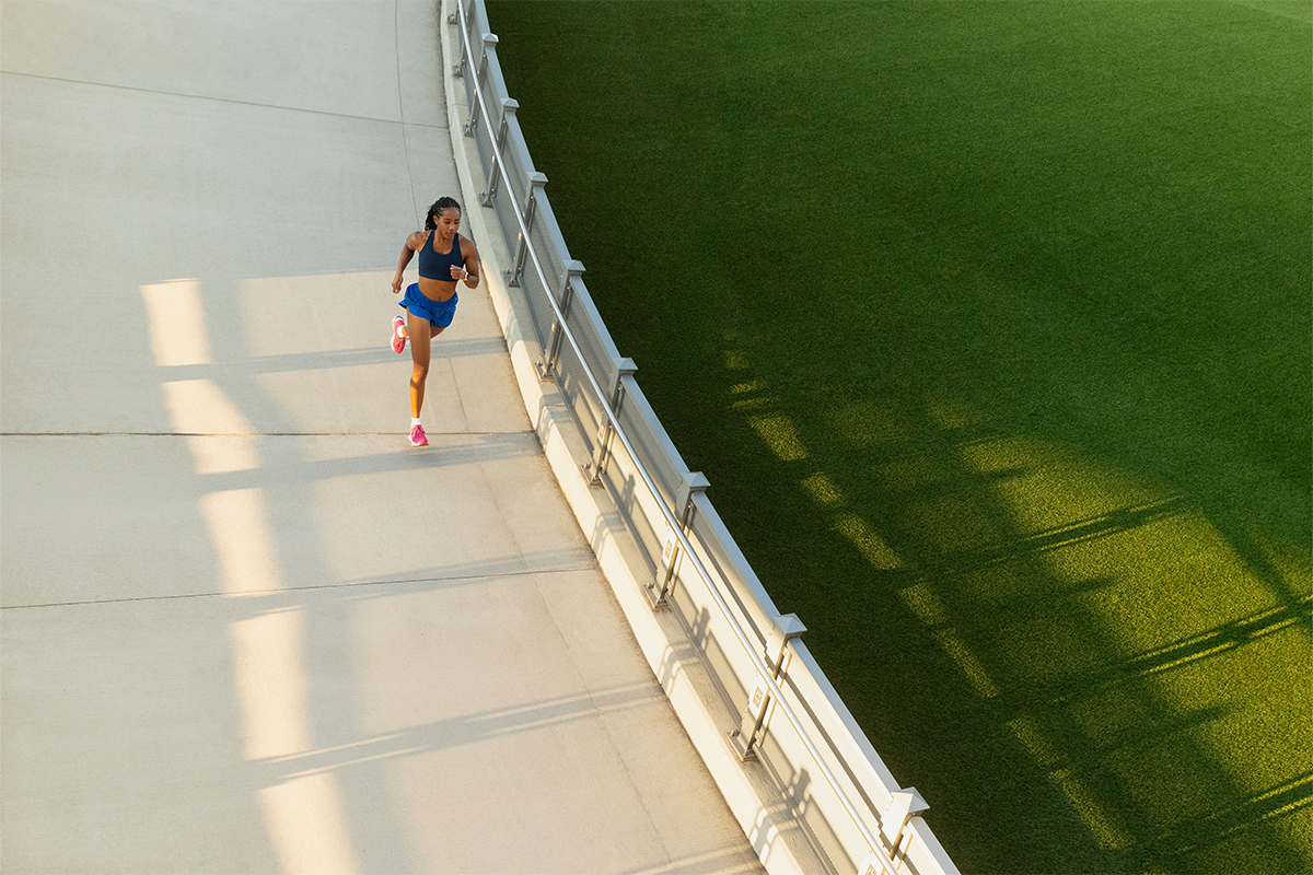 A woman runs alongside a fence that divides pavement and green space.