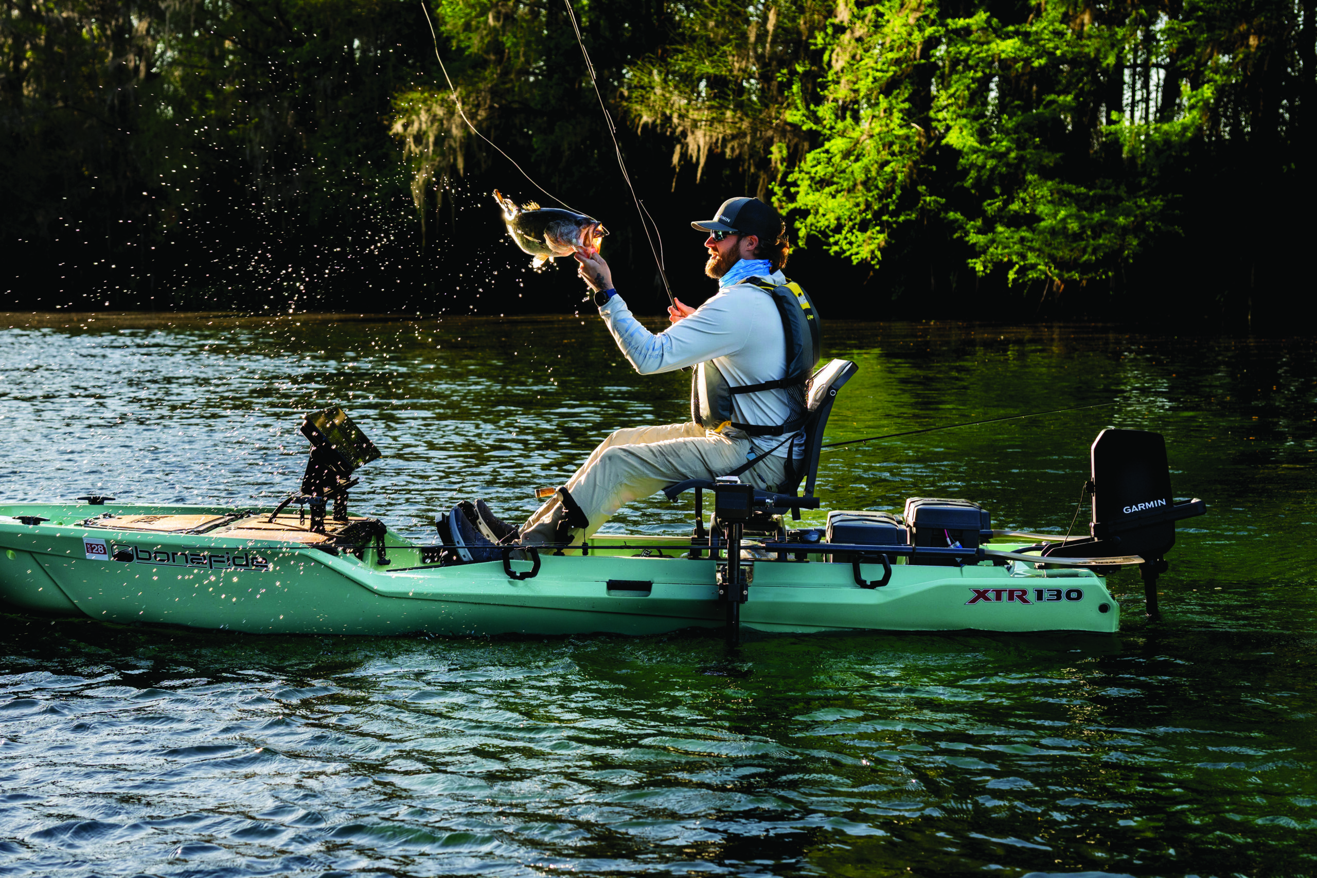 Person sitting on their kayak with a fish in hand and Force Current trolling motor on the back of the kayak.