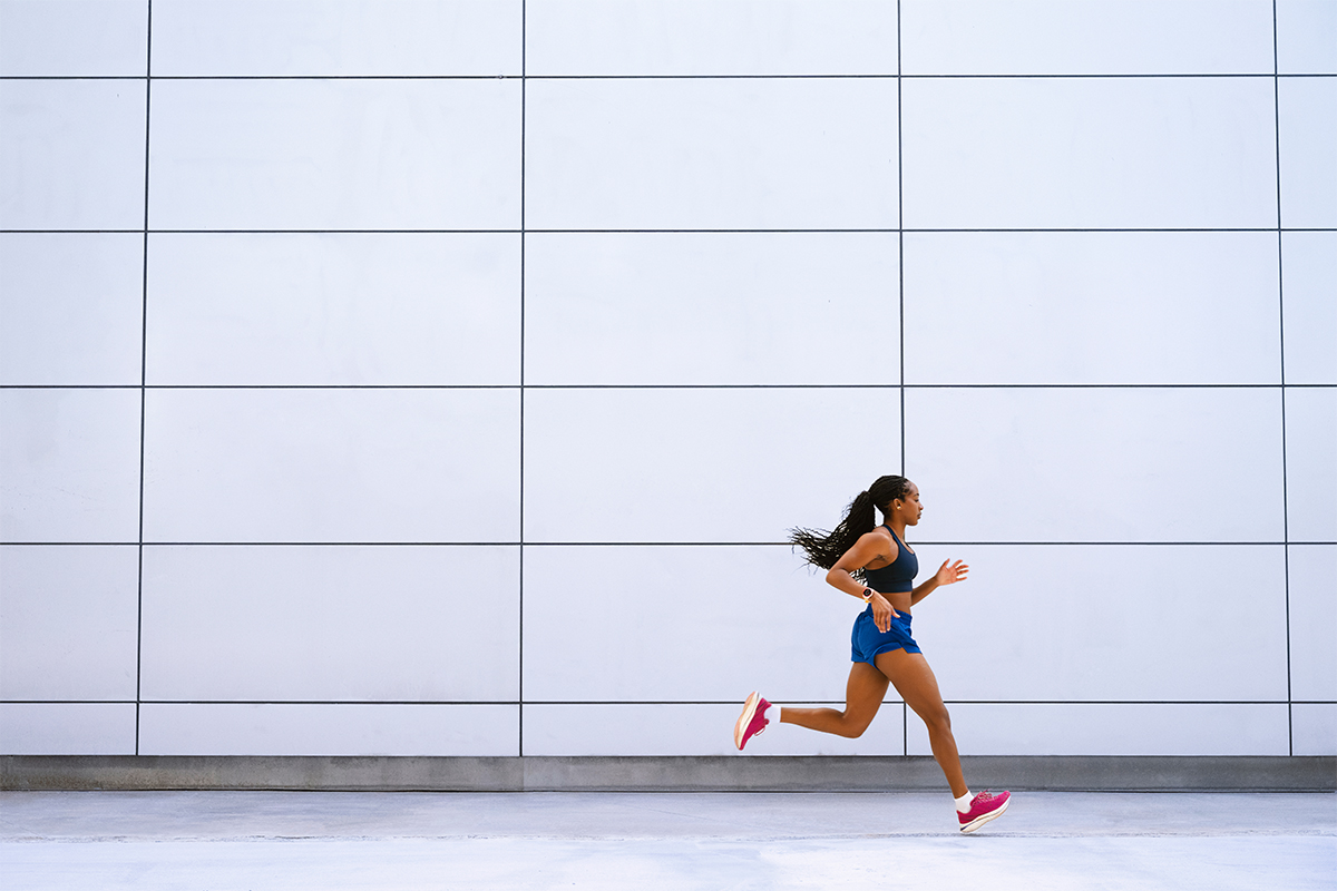 A woman wearing a Garmin Forerunner 970 smartwatch runs in front of a building.