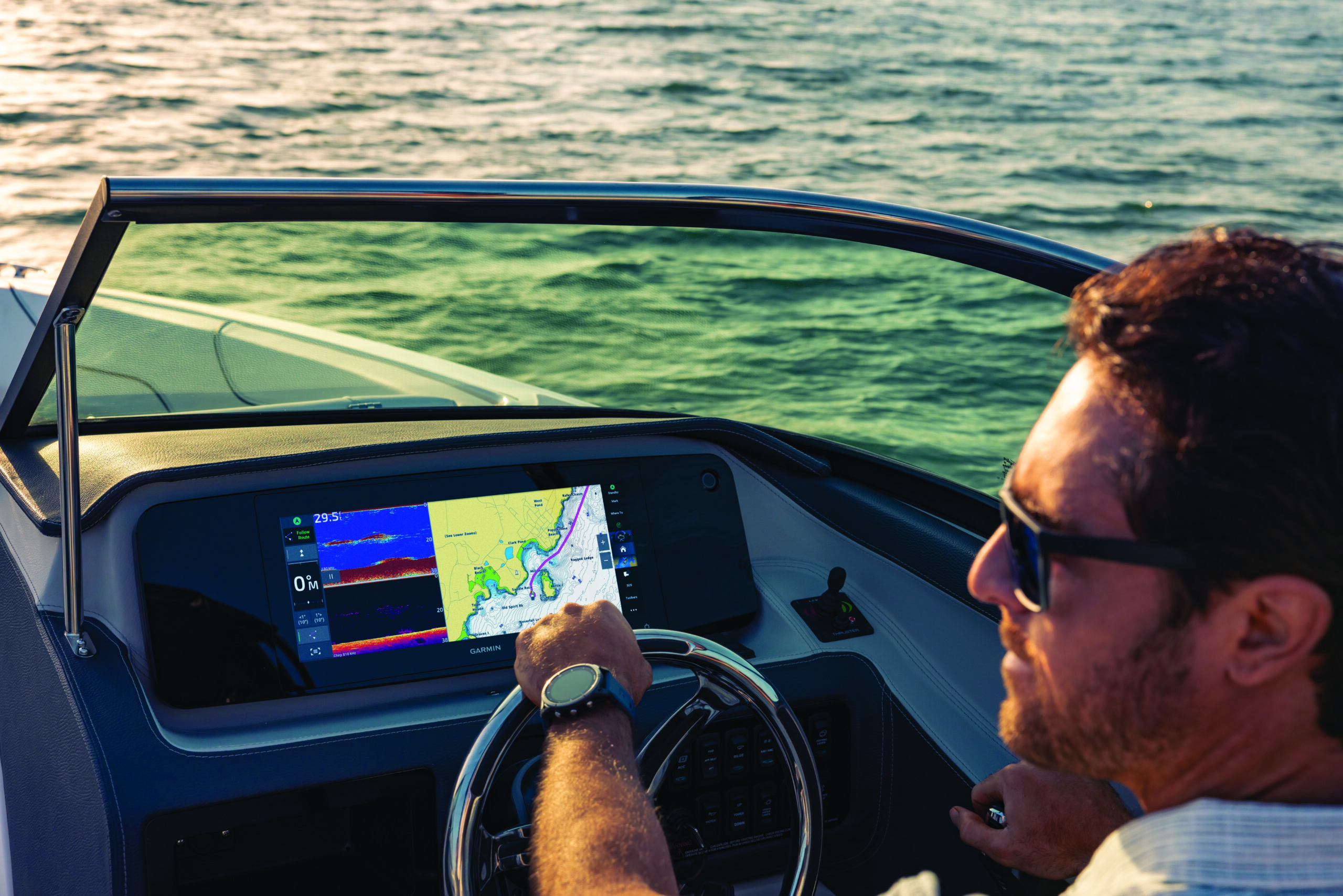 A man at the wheel of a boat with marine charts pulled up on the dashboard.