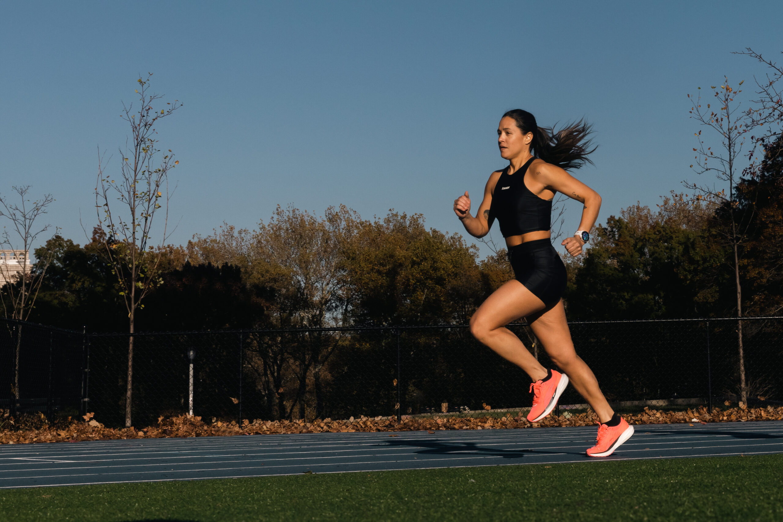 A girl sprinting on a track with trees in the background.