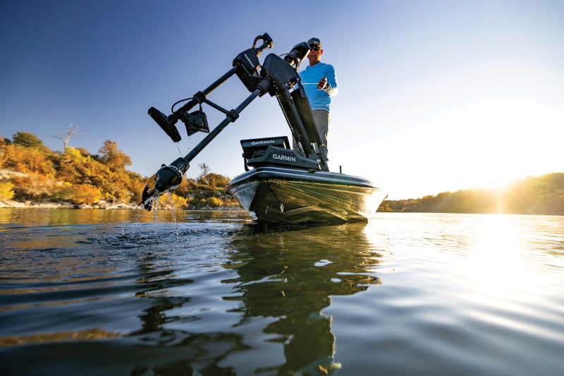 Angler on a boat kneeling to adjust the touchscreen of his Garmin chartplotter while it depicts sonar data. The boat is in the middle of a marsh with more Garmin equipment onboard.